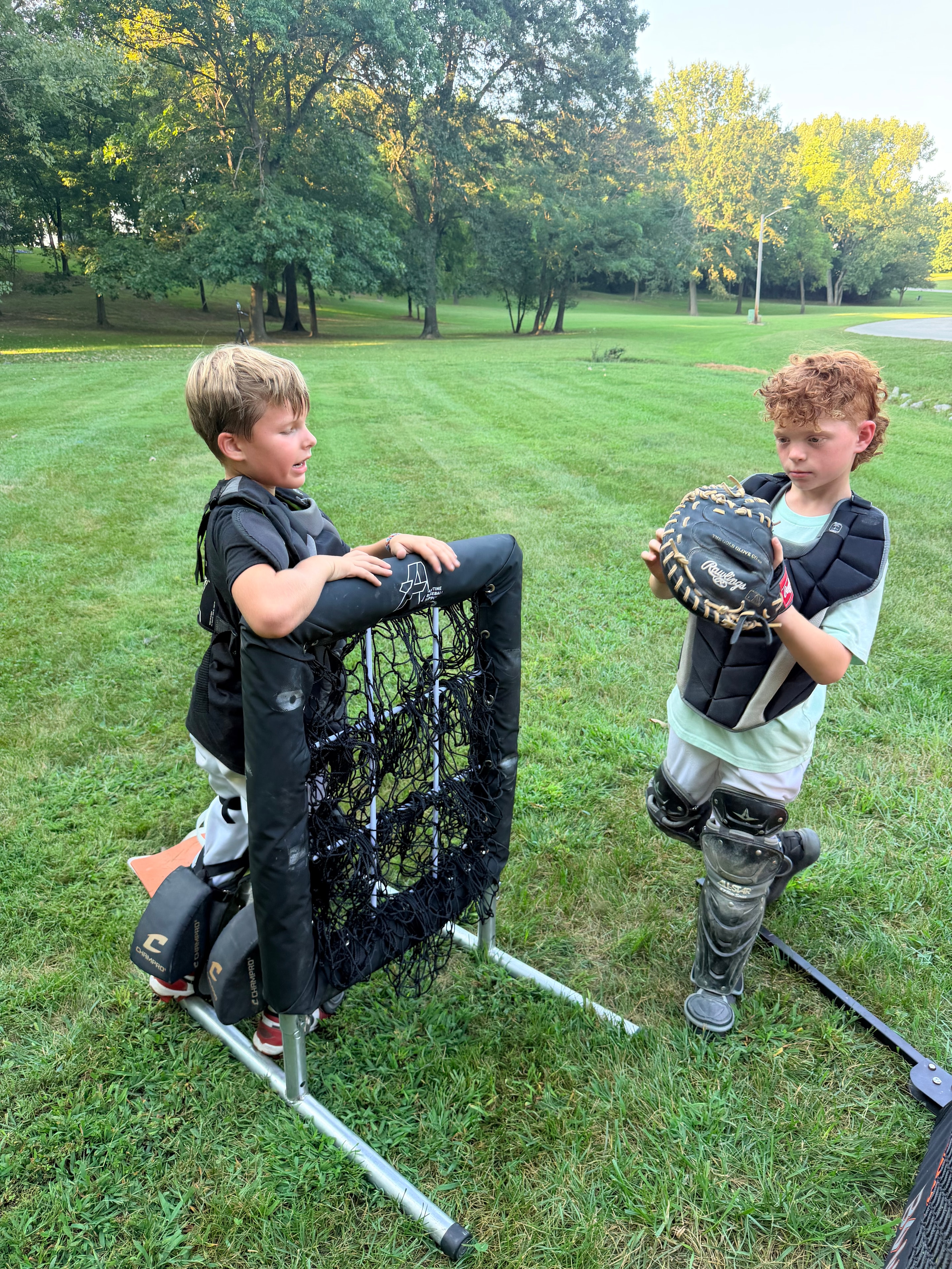 Two young catchers practicing with gear and a training net